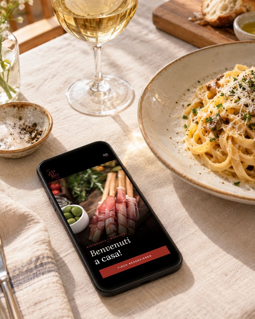 Mobile Restaurant-Website des Emporio Italiano in München auf dem Smartphone neben einem Teller Pasta