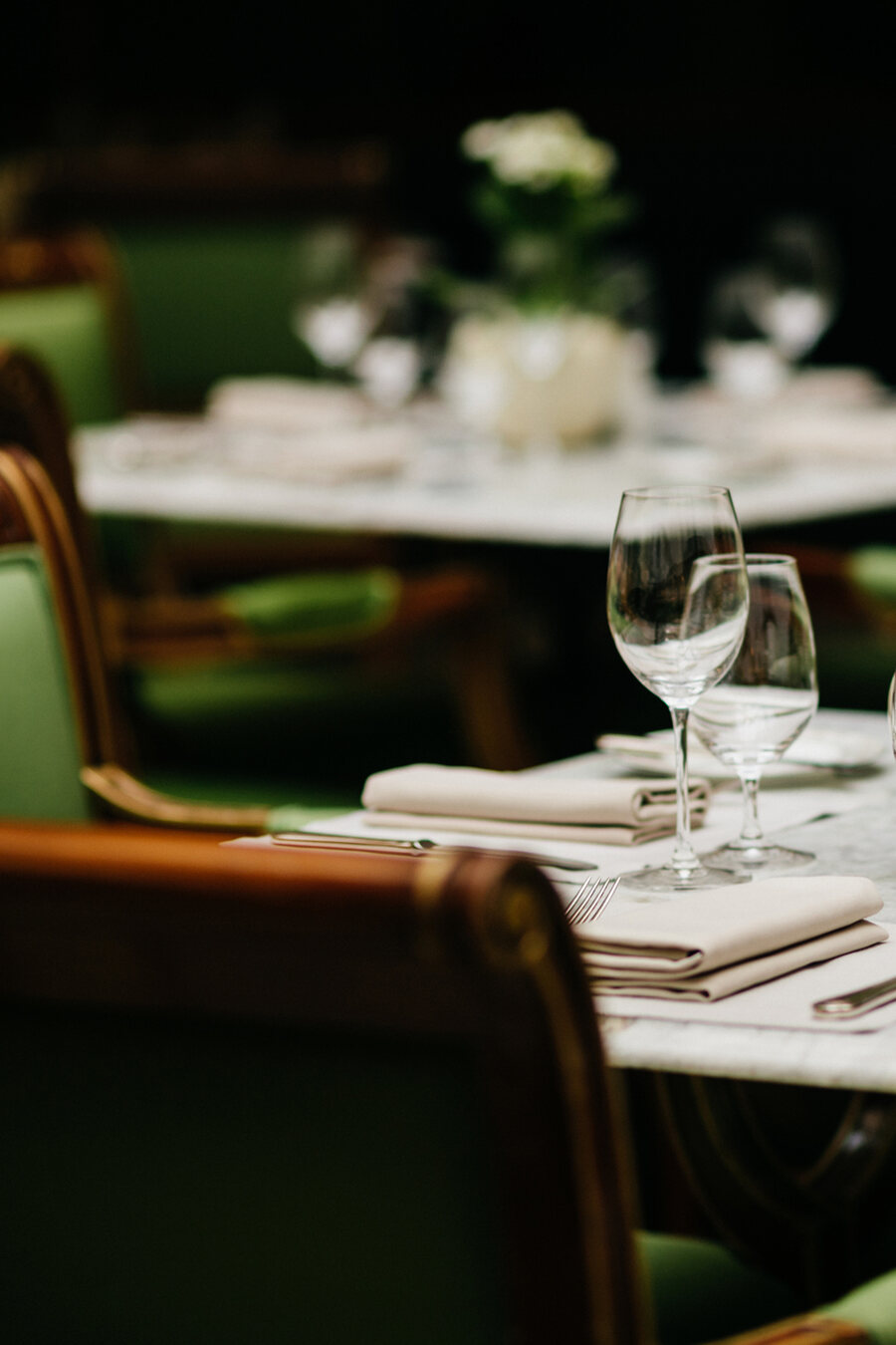 Marmortisch mit gefalteten Servietten, Weingläsern und grünen Polsterstühlen kurz vor dem Abendservice