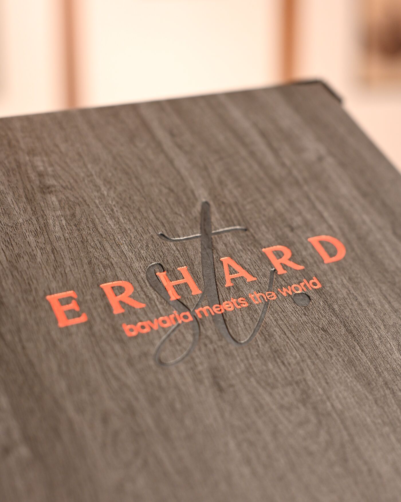 Einband der Speisekarte des Restaurants St. Erhard in Regensburg in dunkler Holzoptik mit geprägtem Schriftzug ERHARD und dem Zusatz bavaria meets the world in Orangerot