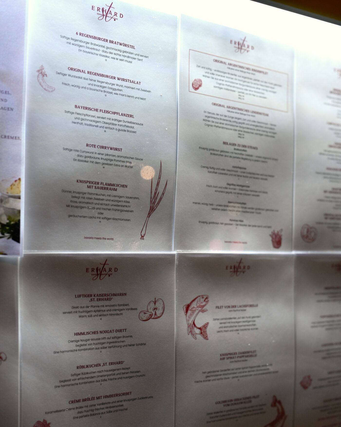 Echte Speisekarte des Restaurants St. Erhard in Regensburg im beleuchteten Schaukasten mit Seiten zu Regensburger Bratwürsteln, Wurstsalat, Kaiserschmarrn und Desserts, rote Illustrationen auf hellem Papier